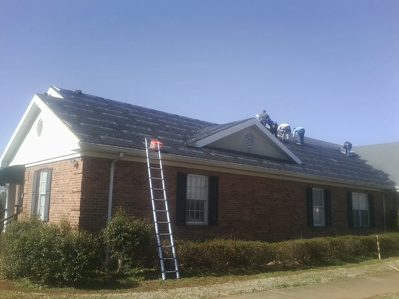 Crew tearing shingles off a brick ranch roof with a ladder set — Emergency Roof Repair work by our crew in Townsend