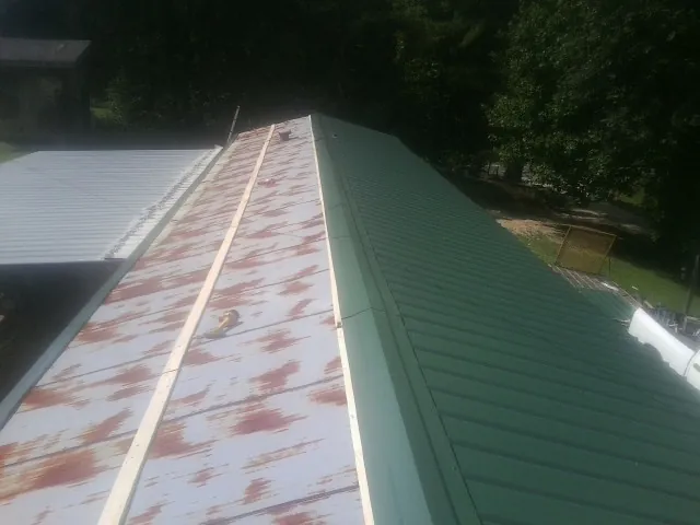 Old rusted panels beside newly installed green metal roofing — Wind Damage Roof Repair by Roofing Brothers in Townsend